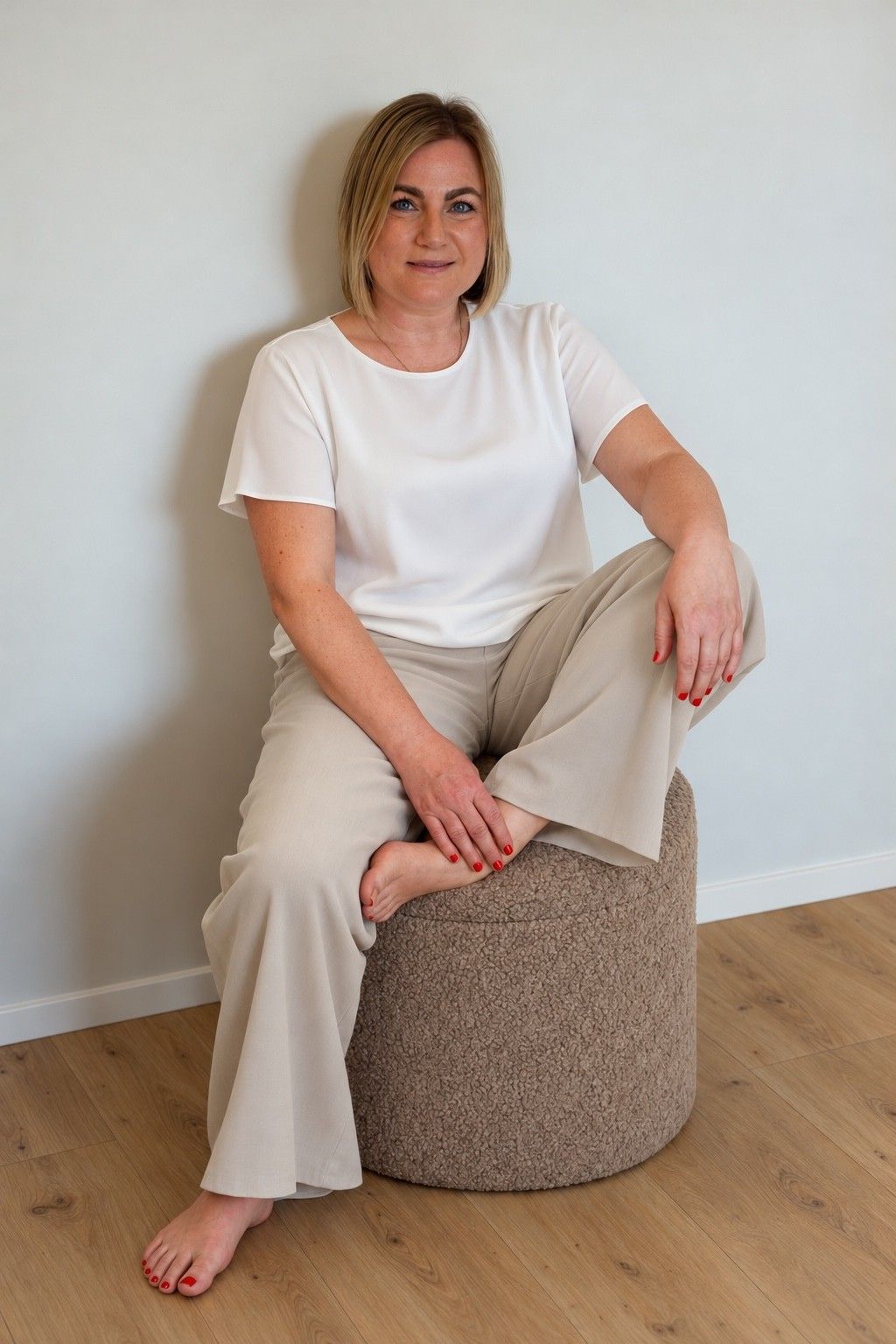 Maike sitzt entspannt auf einem Hocker, einen Fuß angezogen, und lächelt